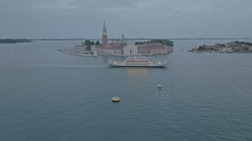 Aerial view of the historic San Giorgio Maggiore island with a ferry crossing the lagoon under an overcast sky in Venice, Veneto, Italy.