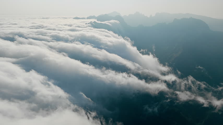 Aerial view of moving clouds beside mountain ridge. Cloud cover partially obscures valley below
