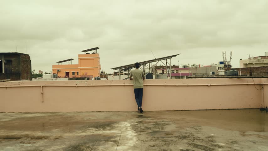 wide view of a man standing on a rooftop terrace during cloudy overcast monsoon weather. back shot