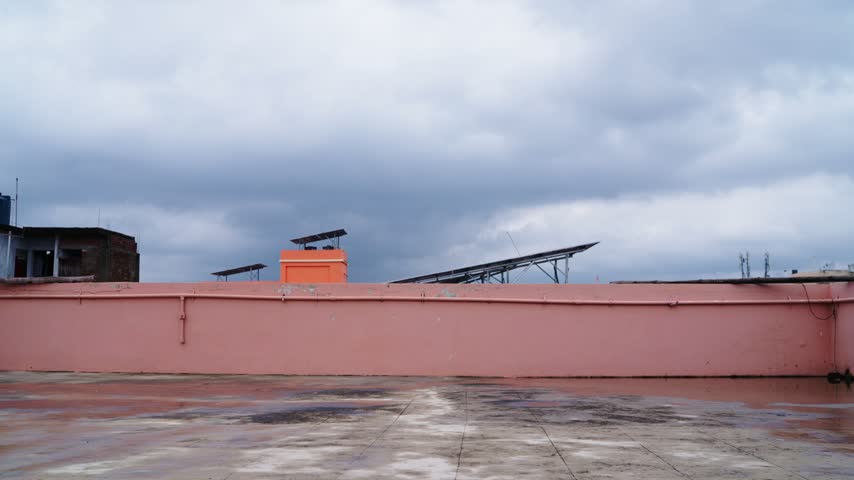 wide view of a man standing on a rooftop terrace during cloudy overcast monsoon weather. back shot