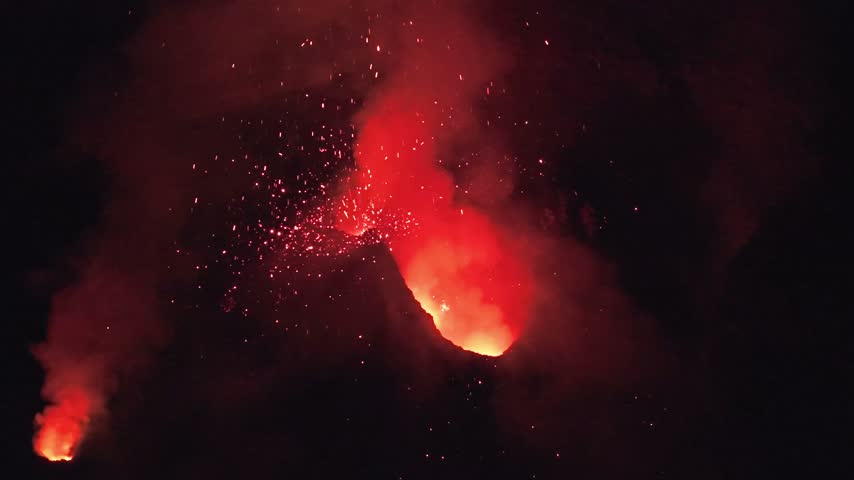 Aerial view of Stromboli volcano erupting at night with glowing lava and sparks illuminating the dark sky in Stromboli, Sicily, Italy.