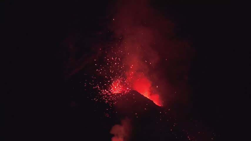 Aerial view of Stromboli volcano erupting at night with glowing lava and sparks illuminating the dark sky in Stromboli, Sicily, Italy.