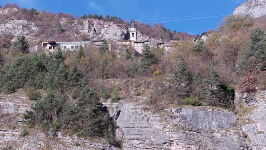 Aerial view of a historic village perched on a rocky cliffside with a church tower and dense forest in Pordenone, Friuli-Venezia Giulia, Italy.