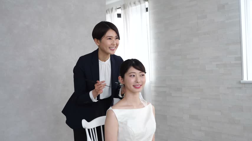 Smiling Asian bride getting her hair styled for wedding