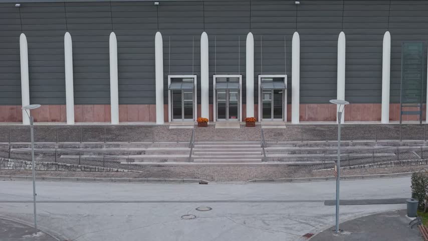 Aerial view of modern building facade with vertical white columns and glass doors in Longarone, Veneto, Italy.