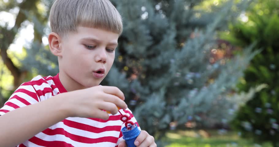 Cute little boy blowing soap bubbles outdoors