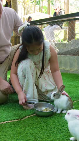 A young girl and her father feed small rabbits from a bowl on green grass