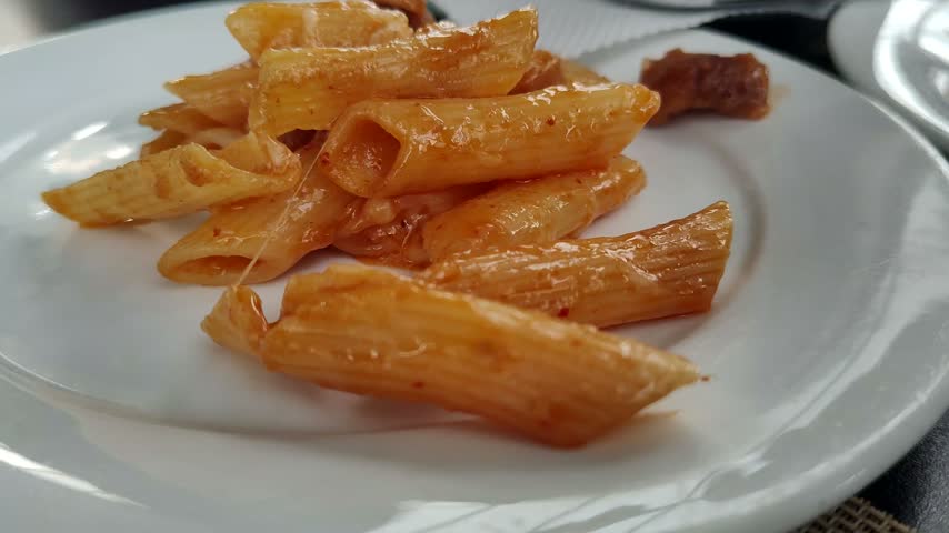 Creamy penne pasta coated in a vibrant tomato sauce with melted, stretchy cheese, served hot on a plate and garnished with a touch of red sauce.
