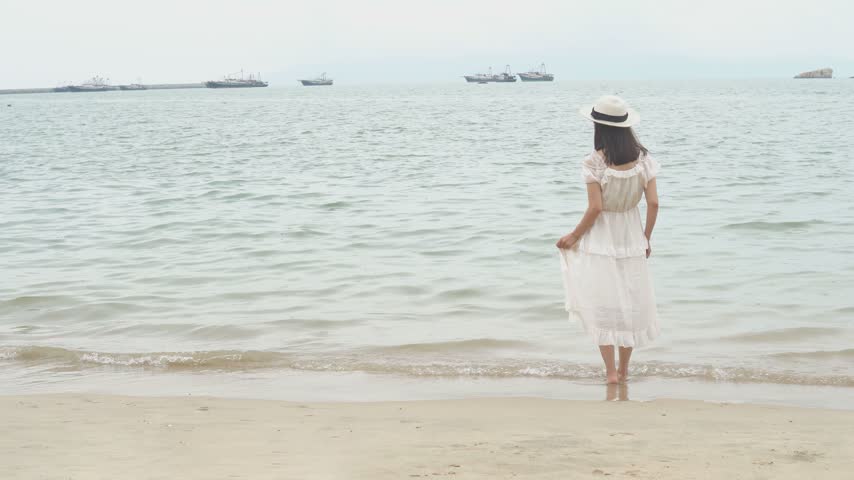Woman in white dress walking along the sandy beach by the sea