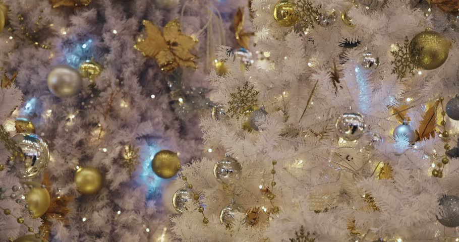 White artificial Christmas tree decorated with gold and silver baubles, glowing lights on branches, festive holiday interior background, seasonal celebration.
