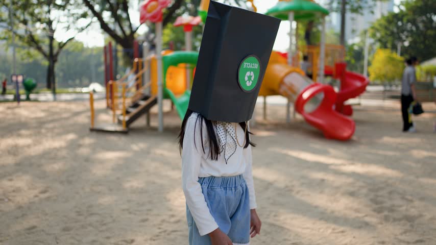 Asian child removes a black recycling bag from her head, smiling at Lumpini Park, Bangkok.