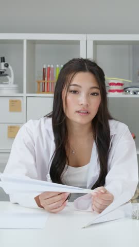 A teenage girl in a white lab coat throws a paper airplane in a classroom.
