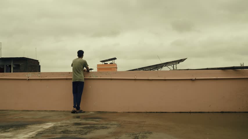 wide view of a man standing on a rooftop terrace during cloudy overcast monsoon weather. back shot