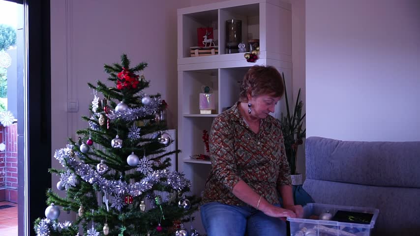 Elderly woman placing a star on top of a christmas tree in her living room during holidays