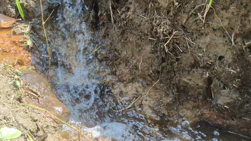 Fast flowing muddy water stream and small waterfall in a rural landscape