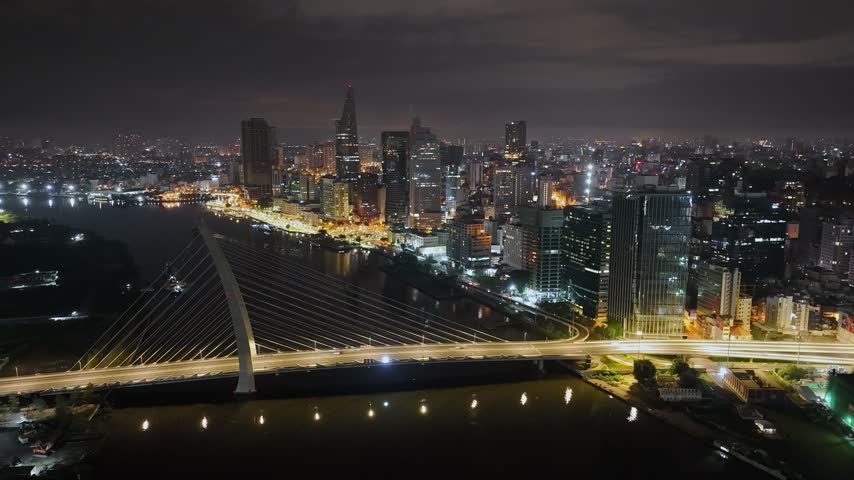 aerial night cityscape with Ba Son Bridge cables in the foreground, the Saigon River below and illuminated downtown skyscrapers across the waterfront