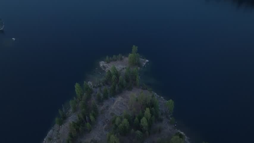 Aerial drone footage captures a scenic wooded peninsula extending into the deep blue tranquil waters of a serene mountain lake at dusk