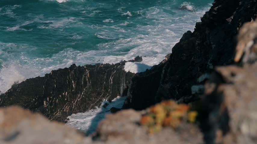 Sea water cascading off a dark rock ledge after a wave, Cabo Sardao, Portugal
