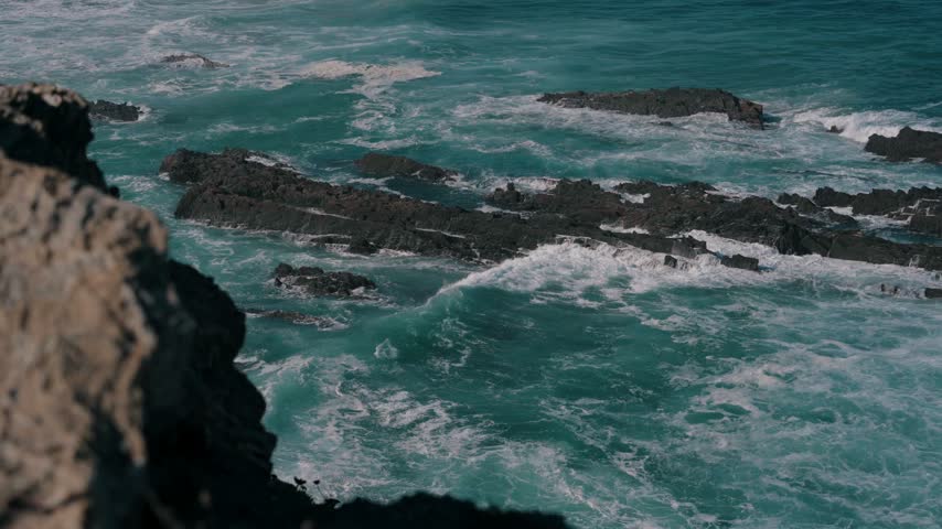 Waves breaking over a dark rock reef framed by cliff rocks, Cabo Sardao, Portugal
