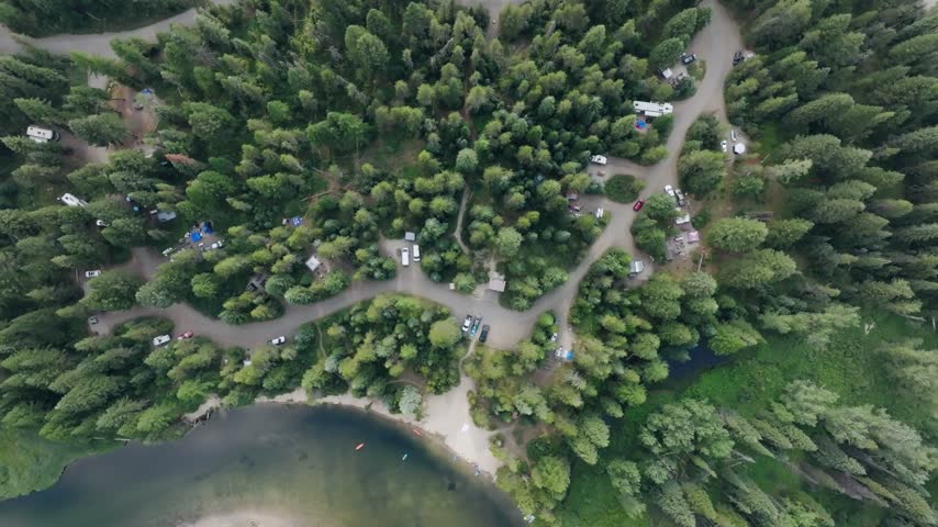 Aerial view of a serene lakeside campground in McCall Idaho featuring pine forests parked recreational vehicles and a sandy beach for leisure and outdoor activities