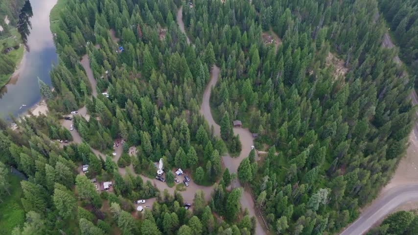 Aerial drone shot capturing a tranquil winding river flowing through a lush evergreen forest in McCall Idaho with a peaceful mountain campground and alpine lake scenery