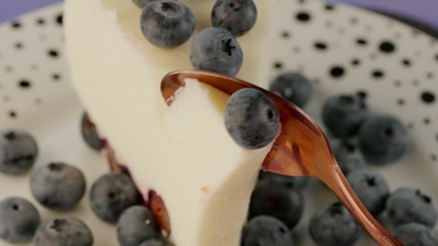 A cottage cheese dessert decorated with fresh blueberries. On the plate lies a piece of cake that is being broken off, revealing its texture, macro photograph.