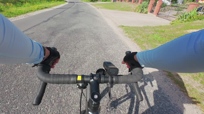 Cyclist rides a bike along a rough country road, with hands on the handlebars. Outdoor cycling and active lifestyle on a sunny day.