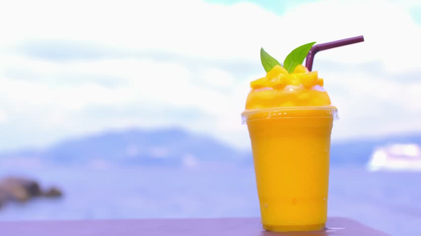 Smoothie made from fresh mango fruits against the backdrop of a seascape. Fruit and yoghurt ice cream decorated with leaves. Glass of tropical dessert close-up.
