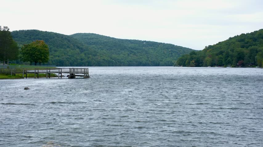 Scenic view of wind rippling across a calm lake with a wooden fishing dock and lush forested hills in Connecticut.