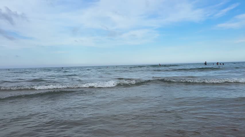 Calm Mediterranean water meets a wide horizon under a blue sky with small figures swimming in the distance in Gandia, Spain.