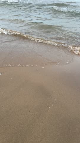 Vertical shot of a soft Mediterranean wave sliding up the sand and sinking back into the shore in Gandia, Spain.