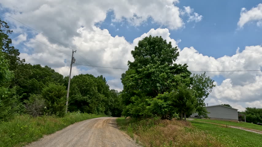 Slow motion vehicle point of view shot traveling down a winding, unpaved gravel country road through dense green forest trees and rolling hills in rural Southern Illinois.