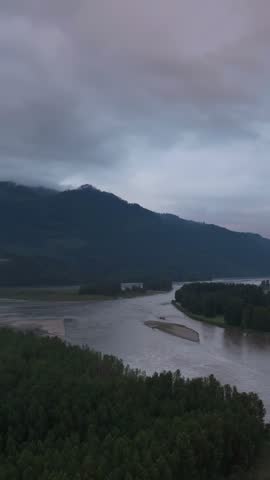 Dramatic Aerial View of a Serene River and Forested Mountains Under Overcast Skies in British Columbia, Canada