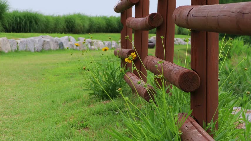 A rustic wooden fence bordering a lush green meadow with wildflowers.