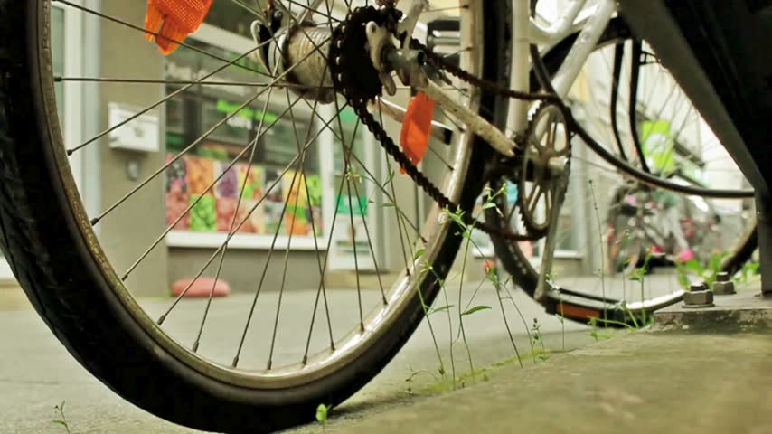 Close up of a bicycle wheel parked on a concrete city sidewalk.