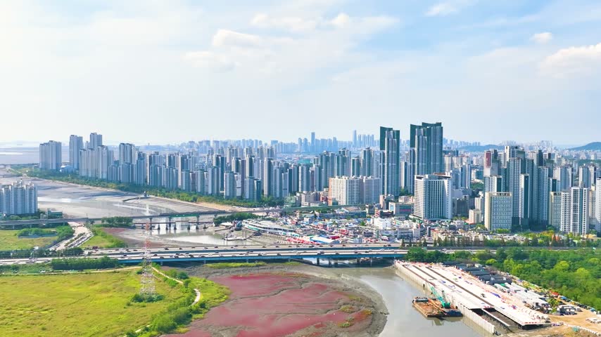 A panoramic 4K cinematic drone view crossing the water from Siheung, capturing the dense high-rise apartment complex and urban skyline of Nonhyeon-dong, Incheon, South Korea. Beautiful waterfront city landscape with smooth camera movement.