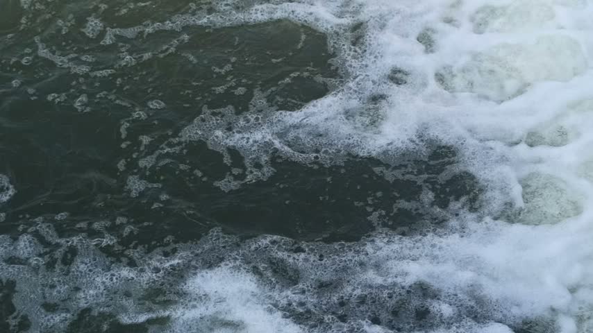 Fast-flowing water rushing over rocks, creating white foam and splashes like a waterfall or dam overflow in a powerful natural river scene.
