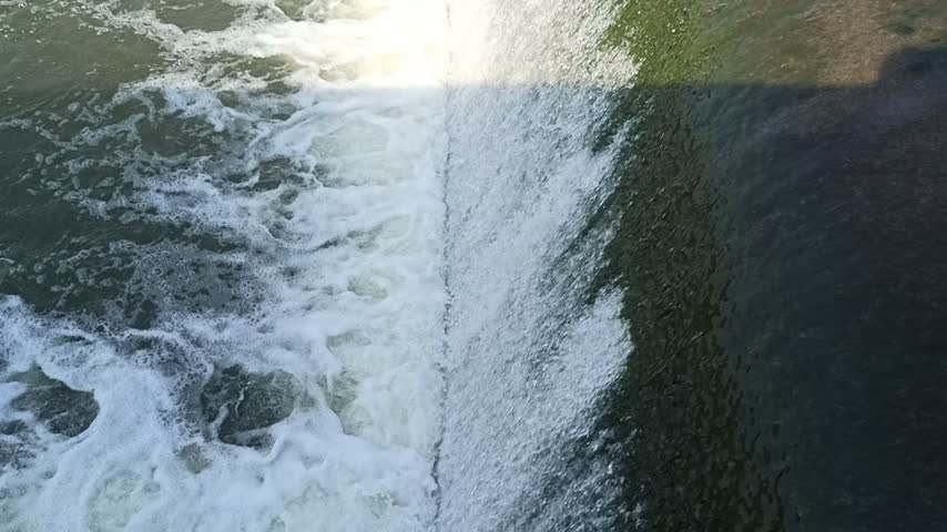 Fast-flowing water rushing over rocks, creating white foam and splashes like a waterfall or dam overflow in a powerful natural river scene.