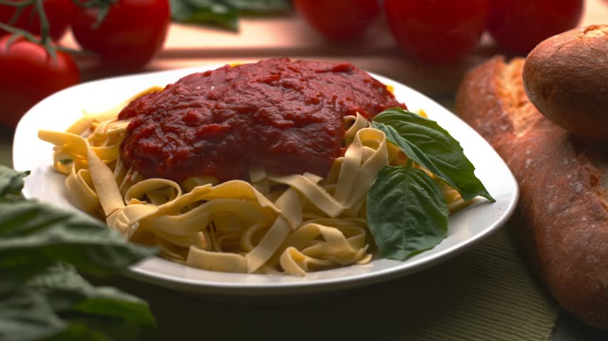 Dynamic overhead shot of delicious fresh pasta with rich red tomato sauce, garnished with green basil leaves and covered with falling grated parmesan cheese. Healthy traditional italian food.