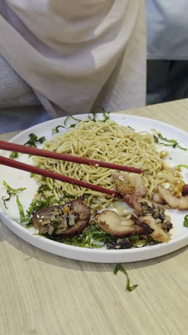A close-up shot of a plate of Asian noodles topped with sliced roasted pork and chopped greens, served on a white plate