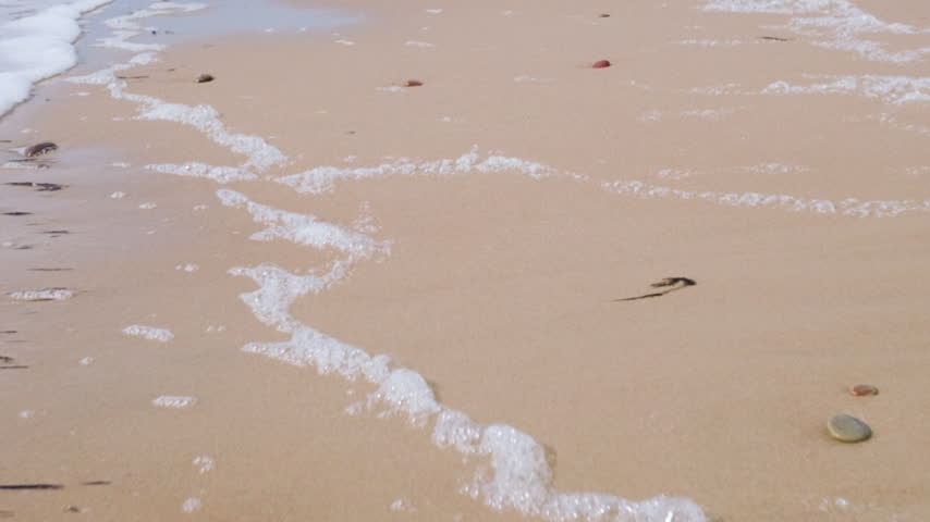 Gentle ocean waves washing over sandy beach with pebbles