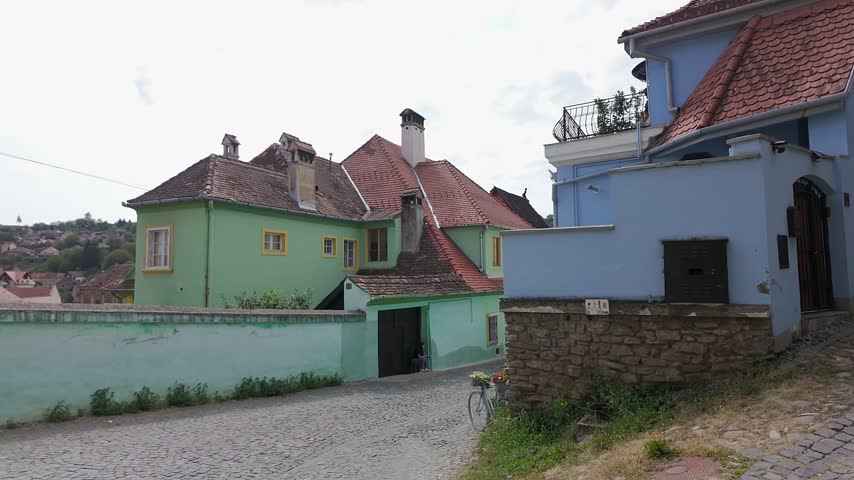 Pastel historic houses and tiled rooftops along a cobblestone street in Sighisoara Romania