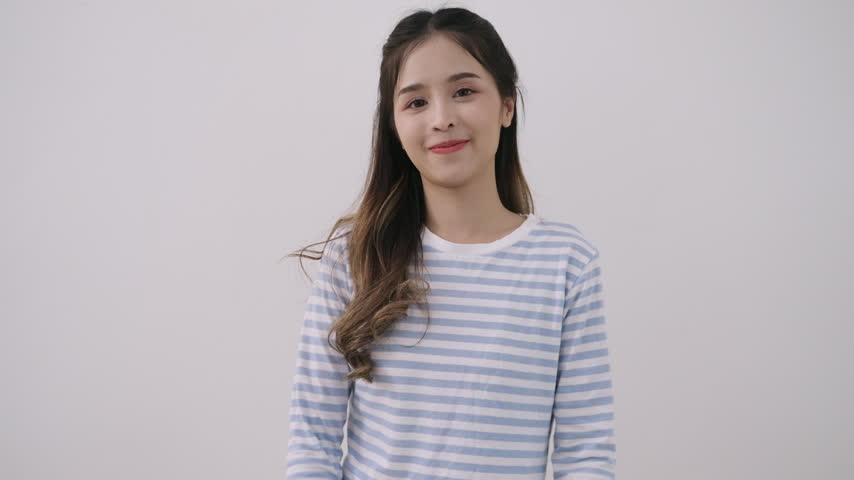 Happy beautiful young Asian woman standing smiling while arms crossed and posing with waving and sending air kiss with her hands while looking at camera with fun and cheerful white studio background. 