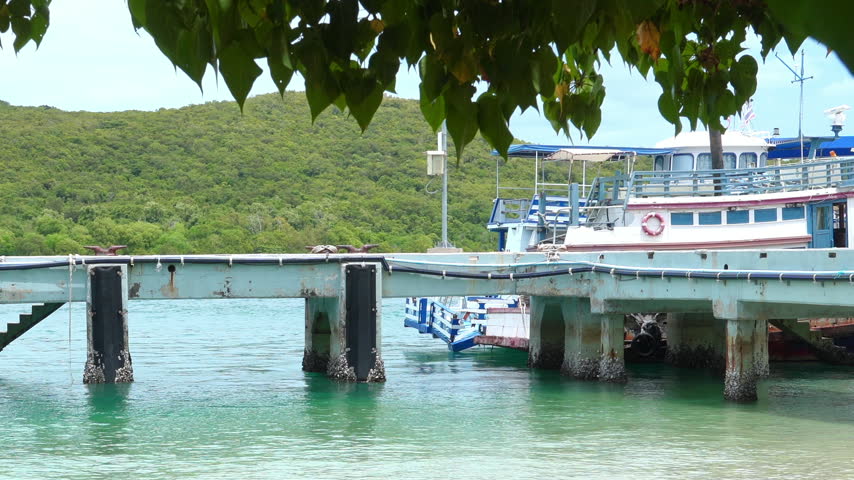 Wooden pier and ferry boat moored at tropical island harbor with clear blue ocean and green hills, clear sky
