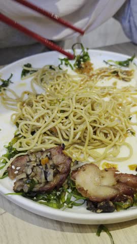 A close-up shot of a plate of Asian noodles topped with sliced roasted pork and chopped greens, served on a white plate