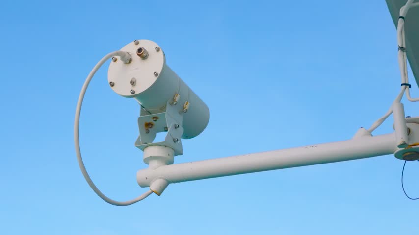 Marine communication equipment and sensor mounted on a ship mast against a clear blue sky background
