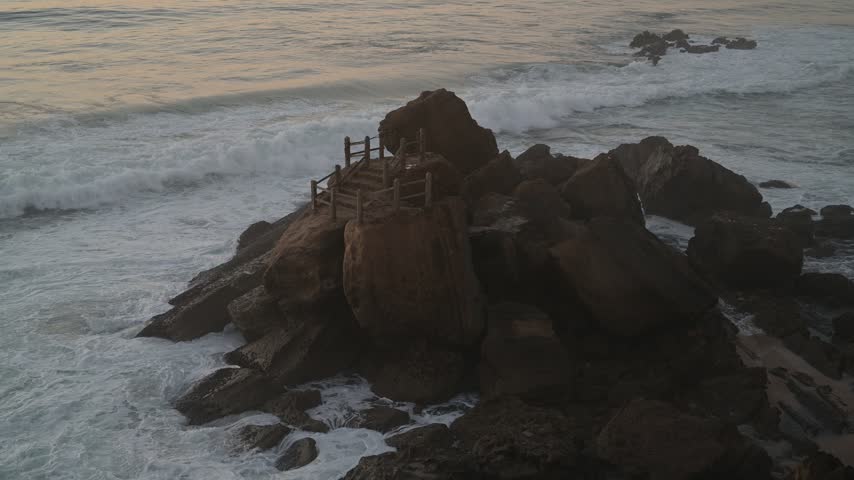 Atlantic surf breaks over rocks beneath a calm horizon at Santa Cruz, Silveira, Portugal.