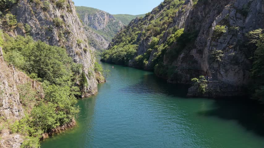 A river flows through a narrow gorge, with steep cliffs and lush trees nearby.