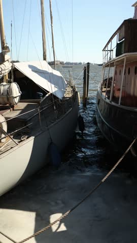 Vertical screen close up of two moored vessels standing side by side at a harbor pier with seawater visible between the hulls mooring ropes and deck structures