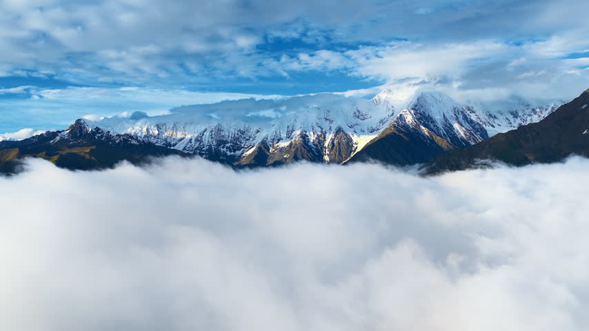Snowy peak of Mount Gongga rises majestically above a dense sea of fluffy white clouds under a bright blue sky during a clear morning.